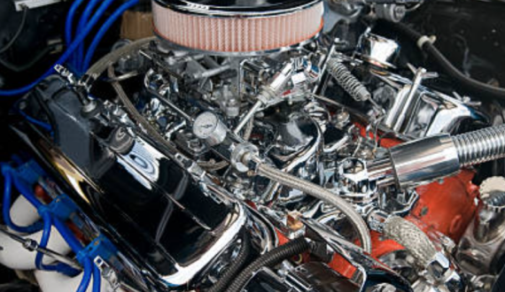 Close-up view of a car engine inside a garage, highlighting various components such as hoses, belts, and air filters. The chrome engine is clean, well-maintained, and customized.