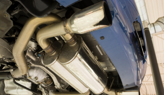 Close-up view of a car's exhaust system and muffler underneath the blue vehicle, showcasing the metal pipes and components in a garage setting, ready for inspection or repair.